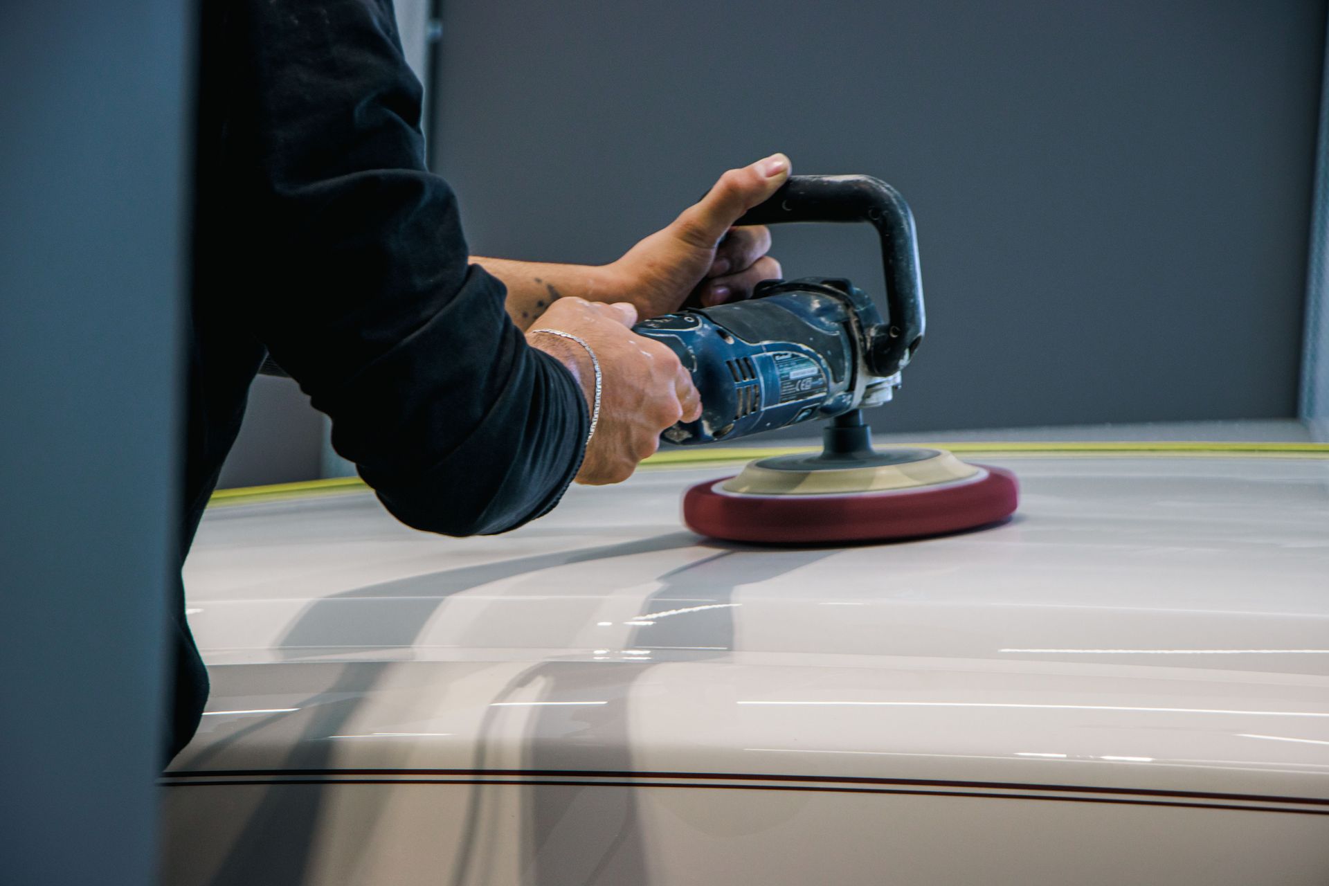 Close-up of hands using a buffer on a car surface, focusing on automotive detailing.